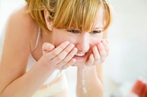 young woman washing her face in a basin and looking herself at the mirror