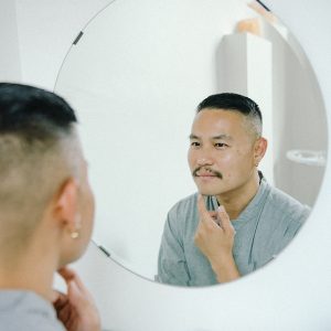 A man looks at his reflection in the mirror as he considers microdermabrasion versus microneedling for his skin