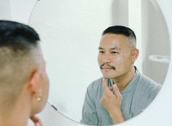 A man looks at his reflection in the mirror as he considers microdermabrasion versus microneedling for his skin